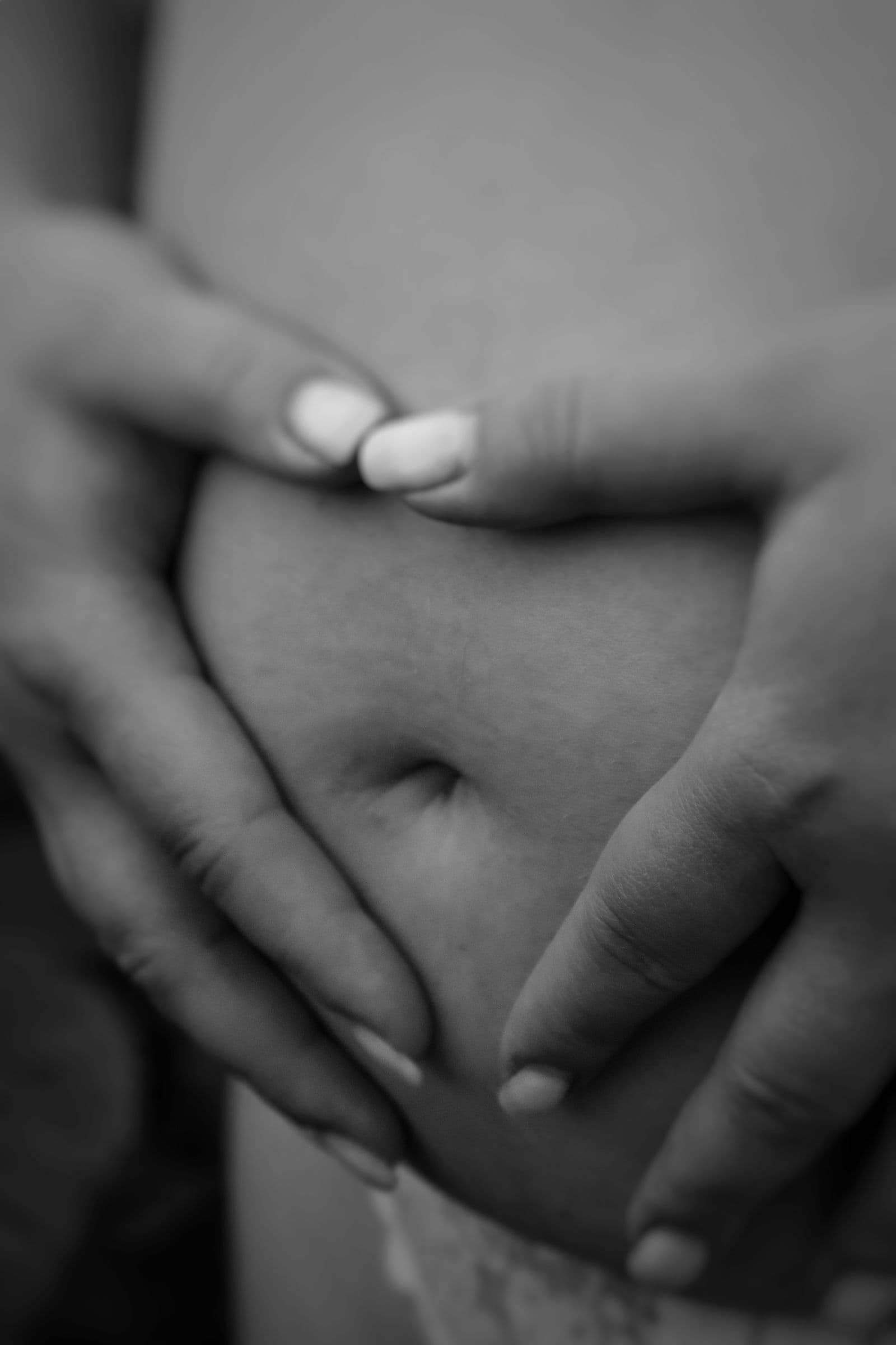 Dłonie splecione na brzuchu kobiety w ciąży, zdjęcie czarno-białe