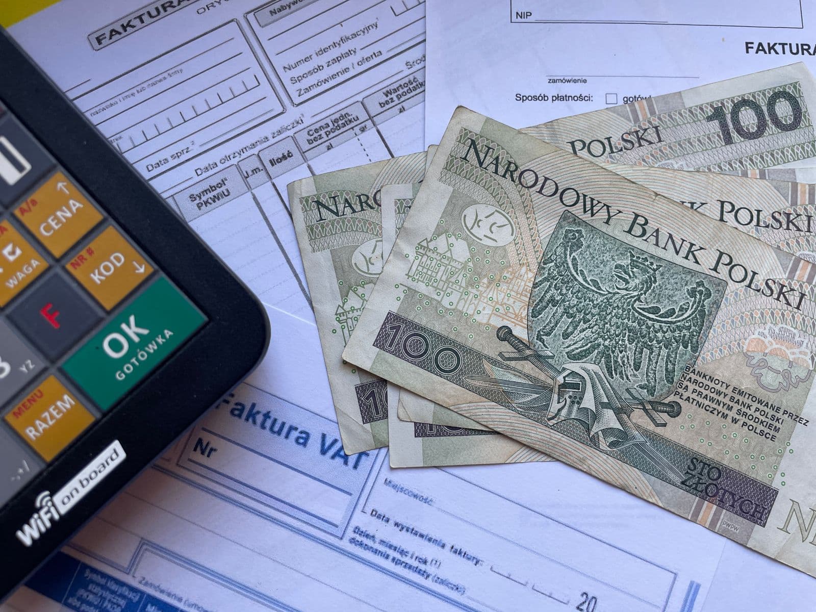 Banknoty stuzłotowe na drukach faktur VAT obok klawiatury kasy fiskalnej